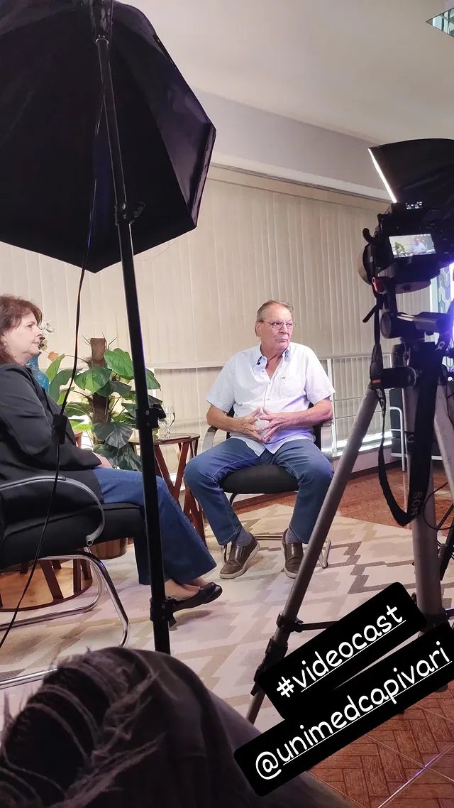 Duas pessoas sentadas para entrevista, com softbox e tripé montados na sala