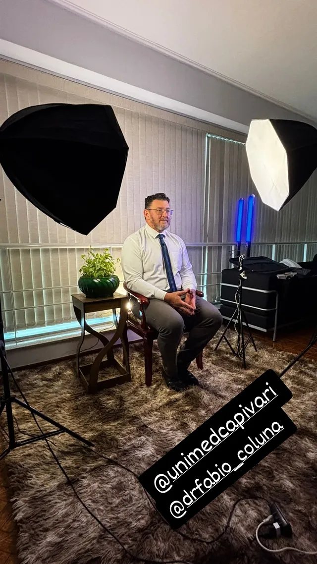 Entrevistado sentado em set montado, com softbox de cada lado e fundo neutro