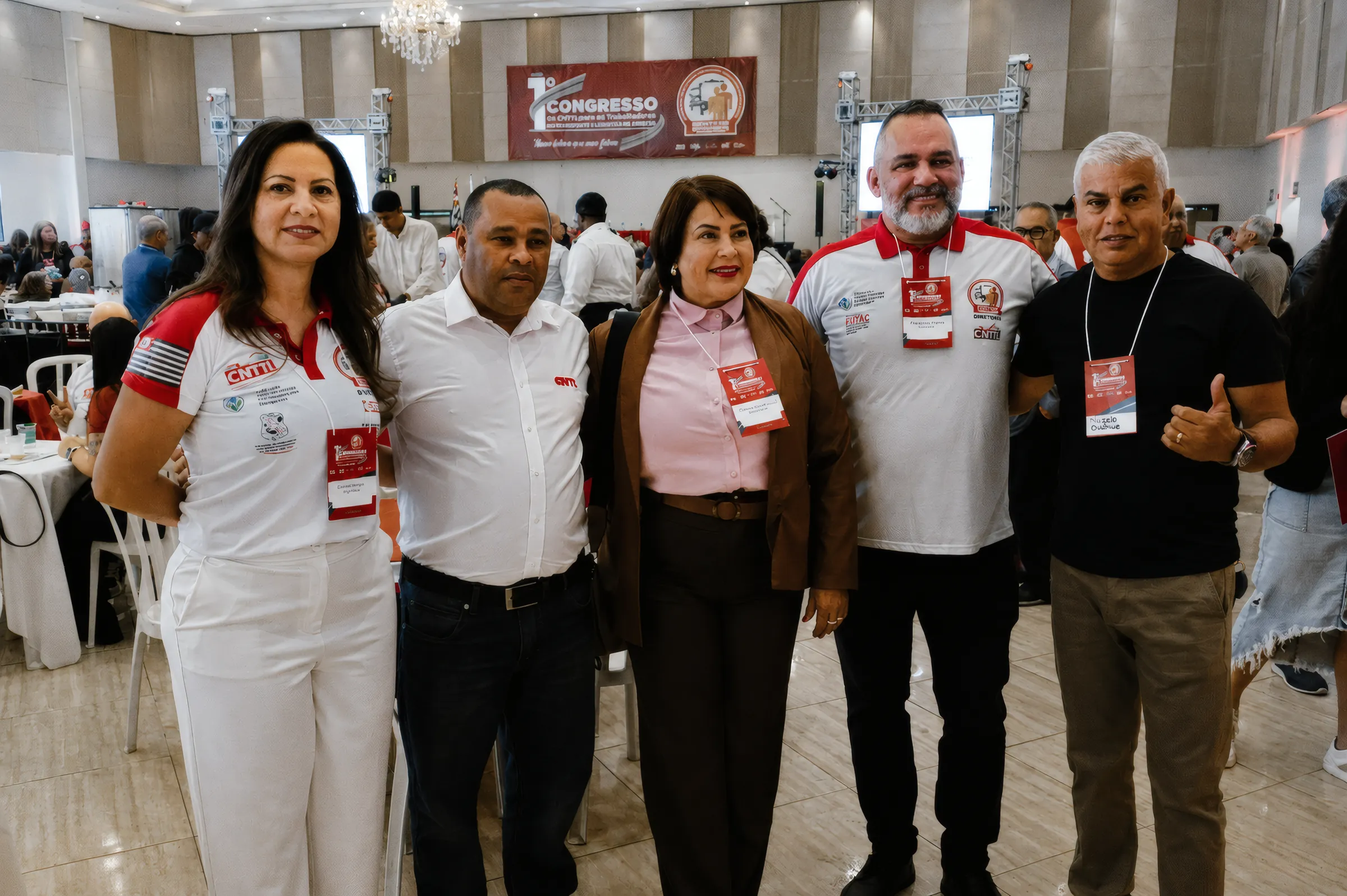 Cinco pessoas com crachá do congresso, posadas no salão, com a faixa do 1º Congresso ao fundo