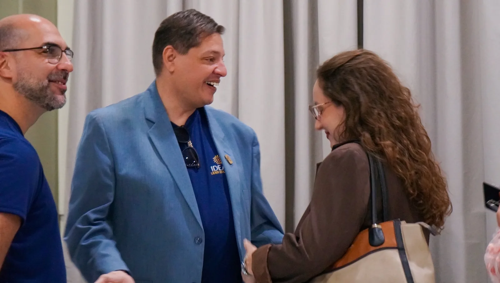 Conversa no salão: participante de blazer azul ri conversando com uma mulher de cabelo cacheado
